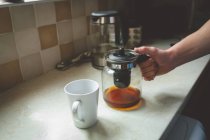 Tarro de filtro de café en mano masculina y taza en encimera de cocina en casa . - foto de stock