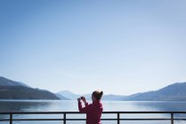 Вид сзади женщины, фотографирующей с мобильного телефона в солнечный день — стоковое фото