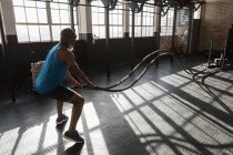 Uomo anziano determinato che fa allenamento con corde cross fit in palestra . — Foto stock