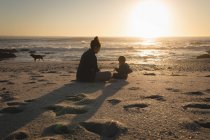Mãe e filho relaxando na areia na praia durante o pôr do sol — Fotografia de Stock