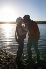 Батьки цілуються, тримаючи дитину біля річки під час заходу сонця . — стокове фото