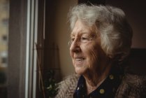 Крупним планом усміхнена старша жінка дивиться з вікна — стокове фото
