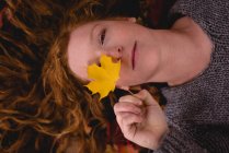 Beautiful woman lying down and holding a maple leaf — Stock Photo