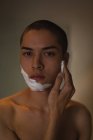 Giovane uomo che applica la crema da barba sul suo viso in bagno — Foto stock