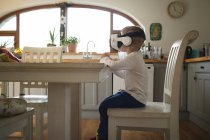 Enfant mâle expérimentant casque de réalité virtuelle dans la cuisine à la maison — Photo de stock