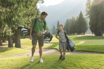 Père et fils avec sac de golf interagissant les uns avec les autres dans le cours — Photo de stock