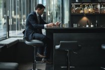 Geschäftsmann benutzt Handy, während er Whiskey am Hotelschalter trinkt — Stockfoto