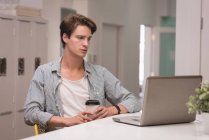 Executivo usando laptop enquanto toma café no escritório criativo — Fotografia de Stock