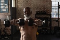 Homme âgé déterminé à faire de l'exercice avec des haltères dans un studio de fitness . — Photo de stock