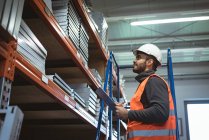 Male worker maintaining record on clipboard in warehouse — Stock Photo