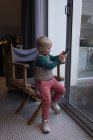Мальчик использует мобильный телефон, сидя на стуле дома . — стоковое фото