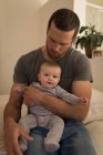 Father holding baby boy while sitting on sofa at home. — Stock Photo