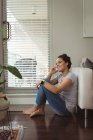 Счастливая женщина разговаривает по мобильному телефону рядом с диваном дома — стоковое фото