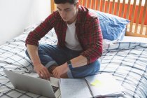 Young man working with laptop while sitting on bed. — Stock Photo