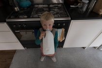 Niño bebiendo leche en la cocina en casa, vista de ángulo alto . - foto de stock