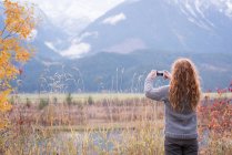 Vue arrière de la femme prenant une photo de montagne avec téléphone portable — Photo de stock