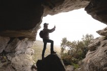 Wanderer steht mit Rucksack am Höhleneingang und fotografiert — Stockfoto