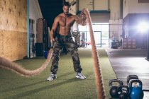 Решительный мускулистый мужчина тренируется с веревкой в фитнес-студии — стоковое фото