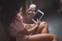 Adolescente usando tableta digital mientras toma café frío en casa . - foto de stock