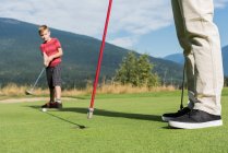 Отец помогает сыну играть в гольф на поле — стоковое фото