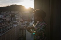 Frau benutzt Handy auf Balkon bei Sonnenuntergang. — Stockfoto