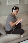 Woman listening to music while writing in notebook at home — Stock Photo