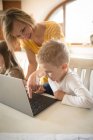Мать учит сына пользоваться ноутбуком дома — стоковое фото