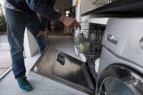 Homem colocando whisker dentro do carrinho da máquina de lavar louça na cozinha em casa . — Fotografia de Stock