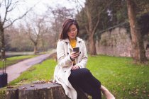 Businesswoman sitting on tree stump and using mobile phone in park — Stock Photo
