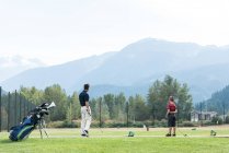 Батько і син, стоячи в полі для гольфу в сонячний день — стокове фото