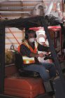 Uomo in abbigliamento da lavoro protettivo seduto in carrello elevatore in fabbrica — Foto stock
