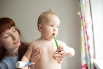 Baby girl brushing her teeth with her mother a thome — Stock Photo