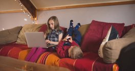 Sibling using multimedia devices on sofa at home — Stock Photo