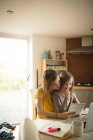 Mother with daughter sitting on chair using digital tablet in kitchen at home — Stock Photo