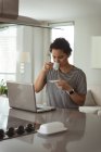 Mulher tomando café enquanto trabalhava no laptop em casa — Fotografia de Stock