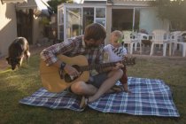 Padre tocando la guitarra con su hijo en el jardín en un día soleado - foto de stock