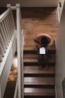 Niño usando tableta digital en las escaleras en casa - foto de stock
