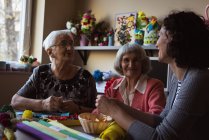 Две пожилые женщины, взаимодействующие с воспитателем в доме престарелых — стоковое фото