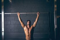 Мускулистый мужчина тренируется на подтягивающем баре в фитнес-студии — стоковое фото