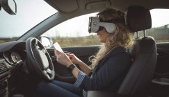 Vista laterale del dirigente femminile utilizzando tablet digitale e auricolare realtà virtuale in un'auto — Foto stock