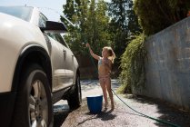 Chica lavando un coche en el garaje exterior en un día soleado - foto de stock