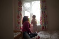 Mãe com sua menina olhando através da janela em casa — Fotografia de Stock