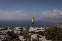 Турист стоит на вершине горы с поднятыми руками в солнечный день — стоковое фото