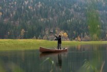 Hombre en canoa lanzando línea de pesca en el río junto a los pastos - foto de stock