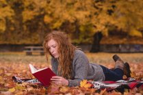 Красива жінка лежить в осінньому парку і читає книгу — стокове фото