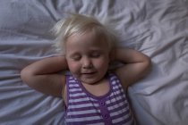 Kleinkind schläft mit den Händen hinter dem Kopf auf dem Bett im Schlafzimmer. — Stockfoto