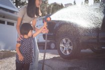 Mãe e filha lavando um carro com um jato de água de alta pressão em um dia ensolarado — Fotografia de Stock