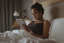 Frau benutzt digitales Tablet auf Bett im Schlafzimmer — Stockfoto