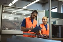 Zwei Arbeiter diskutieren über Klemmbrett in Fabrik — Stockfoto