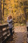 Mujer pelirroja fotografiando en el bosque de otoño - foto de stock